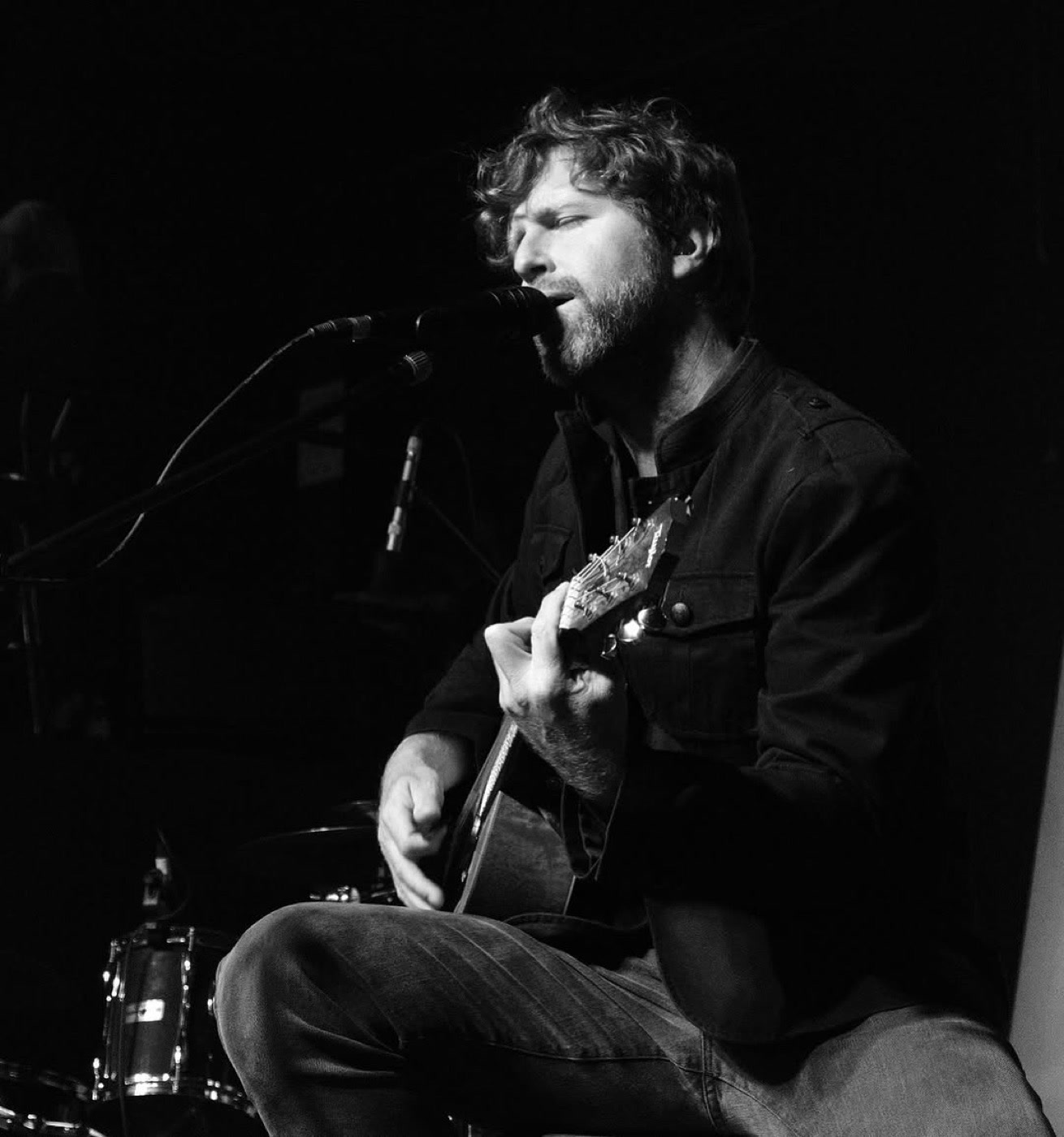 FLØRNAN seated with a guitar, black and white